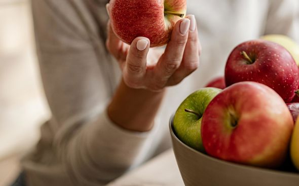 Mujer sostiene una manzana roja en la mano y observa un cuenco con más manzanas frescas