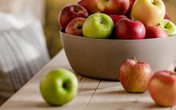 Cuenco con manzanas frescas variadas sobre mesa de madera, montañas visibles detrás