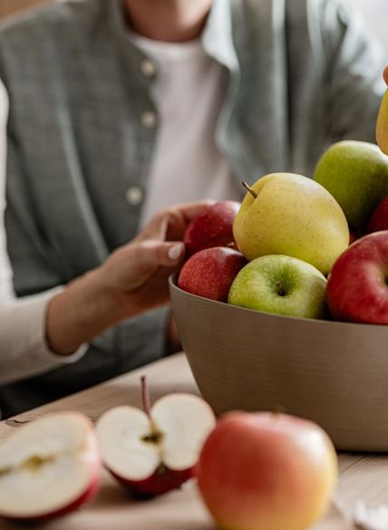 Manzana cortada sobre tabla, al fondo cuenco con manzanas, dos personas y manos que toman una manzana