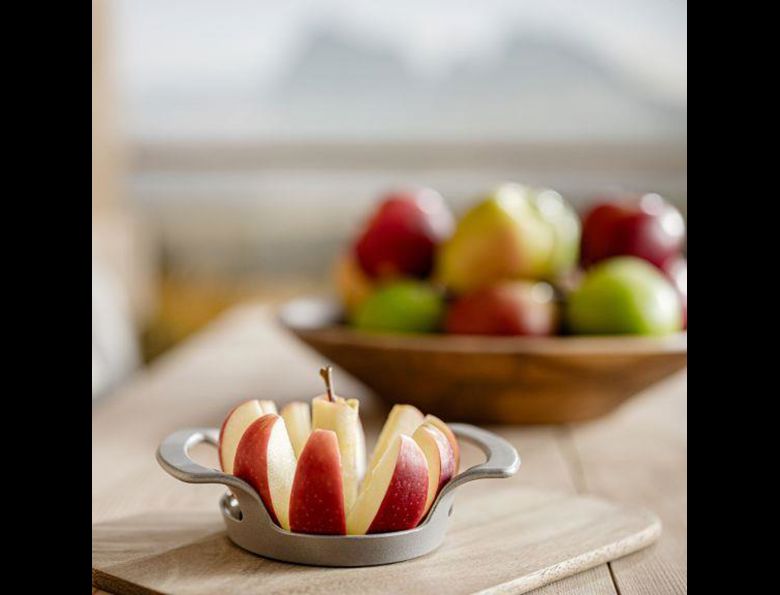 Manzana fresca cortada frente a cuenco con manzanas variadas, montañas visibles al fondo