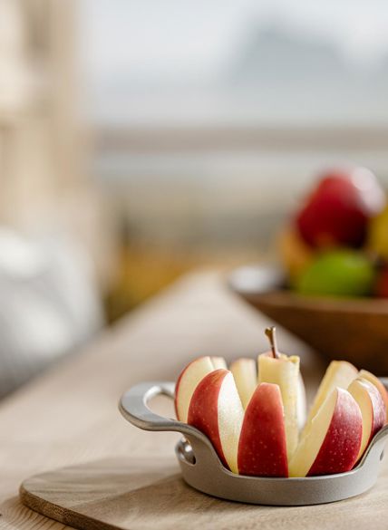 Manzana cortada sobre tabla de madera en primer plano, cuenco con manzanas variadas y montañas al fondo