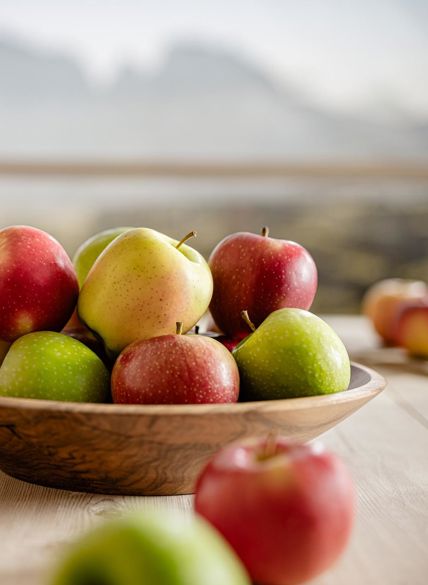 Cuenco de fruta con muchas manzanas de distintas variedades, paisaje montañoso al fondo