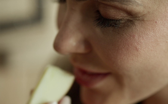 Una mujer huele un trozo de manzana que sostiene en la mano.