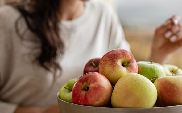 Mujer mira las manzanas frescas en la cesta de frutas y toma una manzana