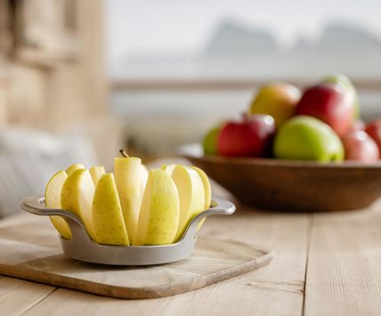 Tagliere con mela a fette in primo piano, sullo sfondo ciotola di mele e montagne
