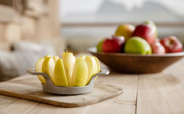 Tabla con manzana en rodajas en primer plano, al fondo cuenco de manzanas y montañas