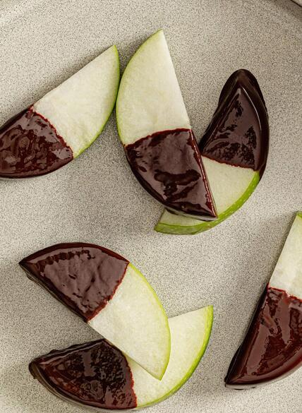 Rodajas de manzana Granny Smith en un plato blanco, algunas parcialmente bañadas en chocolate negro