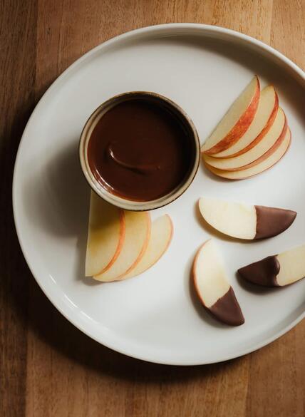 Rodajas de manzana en un plato blanco, algunas parcialmente bañadas en chocolate negro