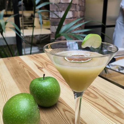Cóctel de manzana con dos manzanas verdes al lado sobre mesa de madera