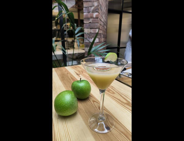 Cóctel de manzana con dos manzanas verdes al lado sobre mesa de madera